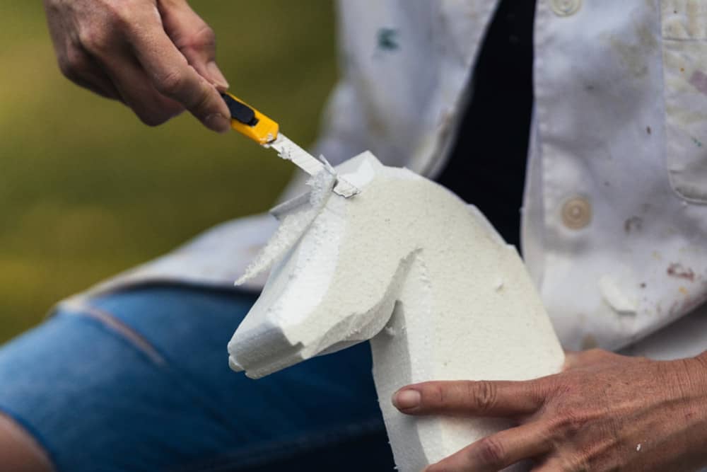 Using a knife to carve a piece of foam into a chess piece.