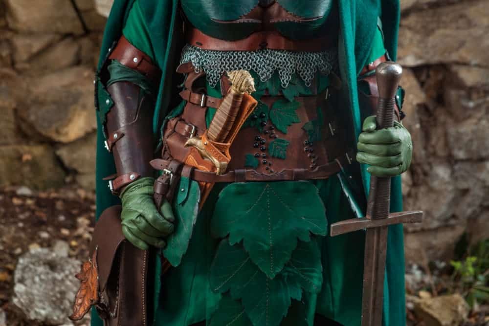 Cosplayer wearing a green cloak and leather accessories.