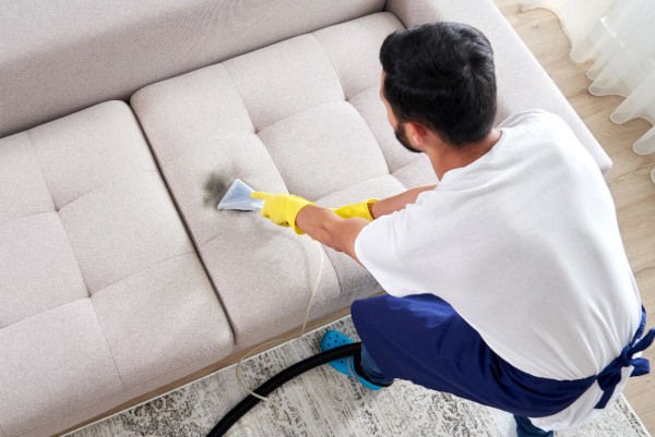 Man cleaning a couch with a steam cleaner.