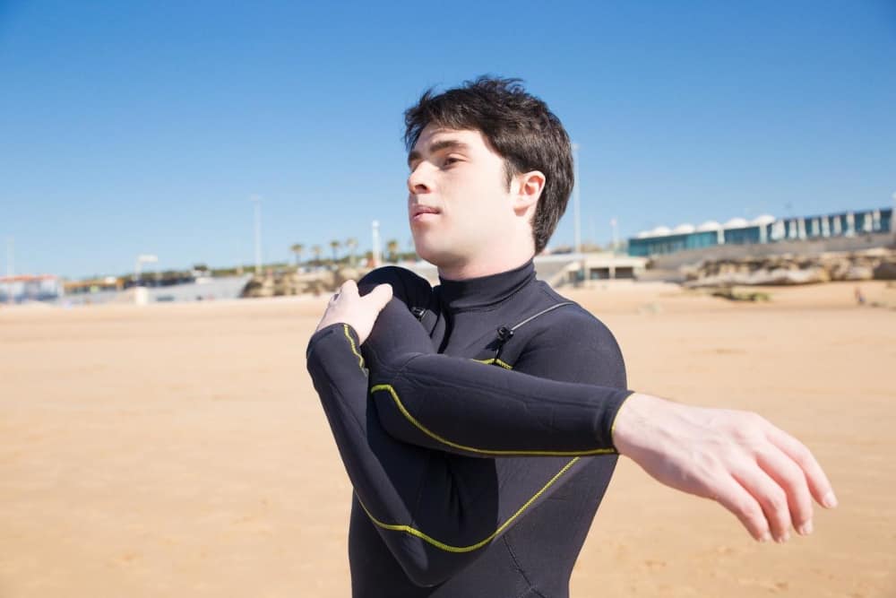 A person wearing a neoprene wetsuit stretching his arm
