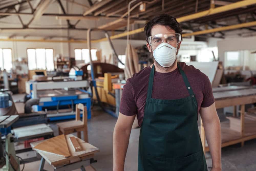 Man in a workshop wearing safety goggles, mask and apron.