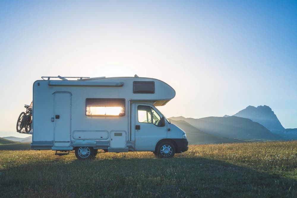 RV parked on grass in front of mountains