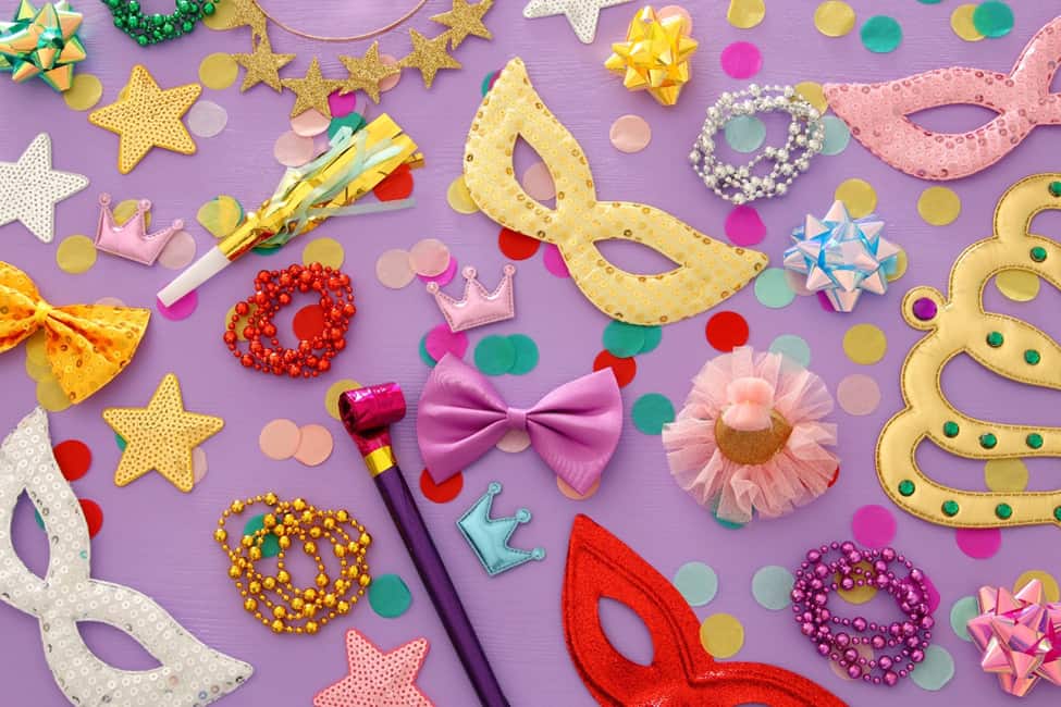 A table full of party supplies including masks, confetti and beads.