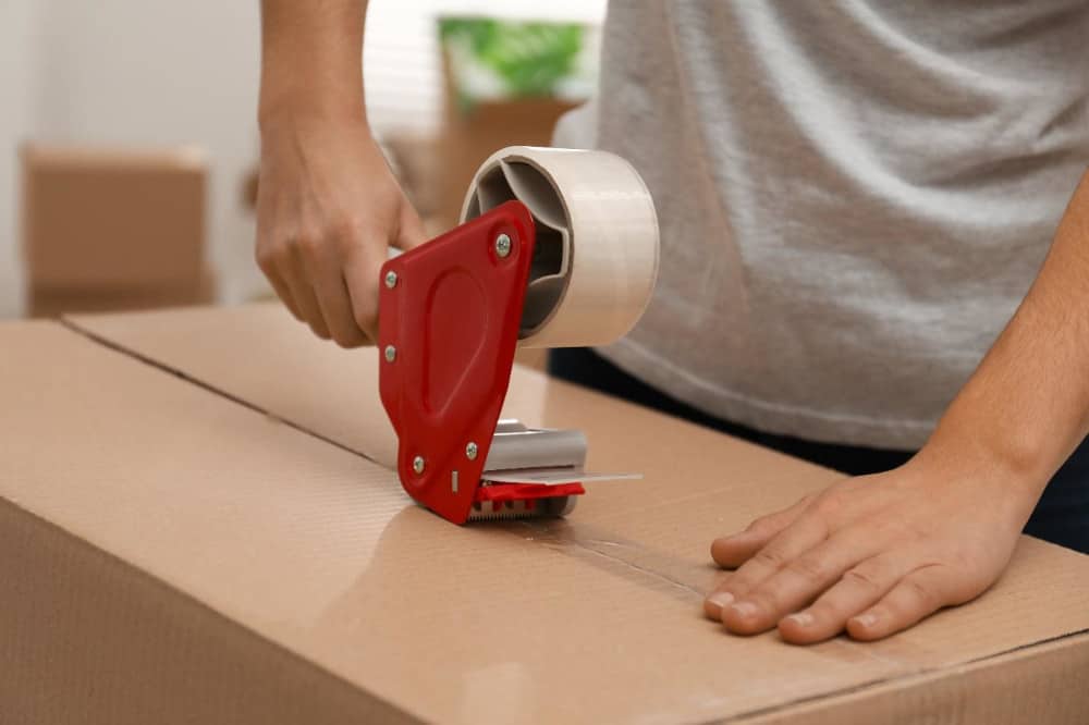 A person sealing a cardboard box with packing tape