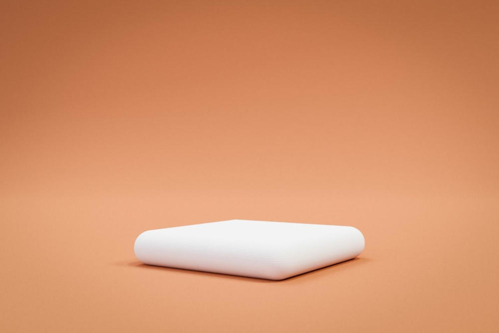 A white square foam pillow against an orange background