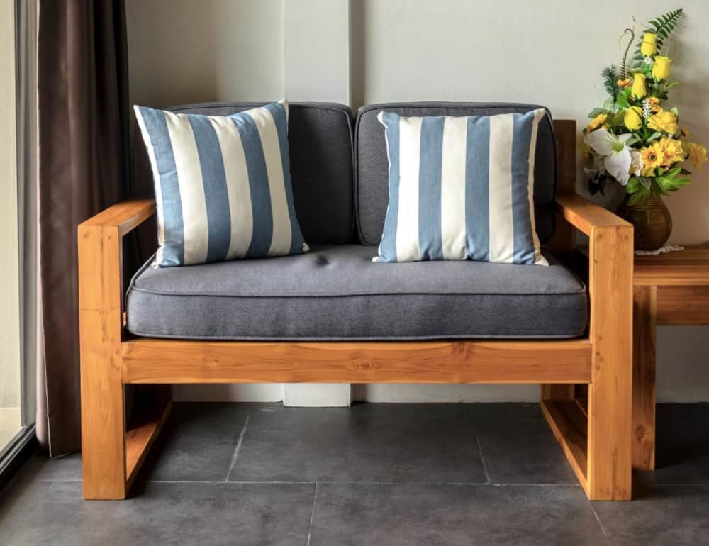 A wooden couch frame with blue cushions and blue striped pillows.