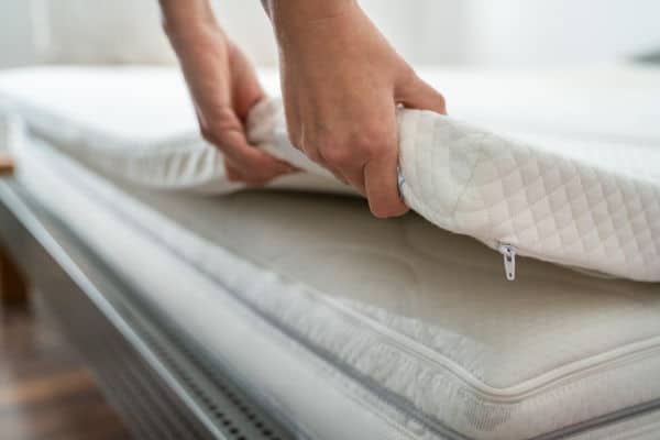 Hands placing a foam topper on a mattress