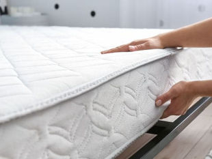 Two hands placing a white mattress on the top of a black bedframe