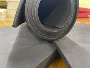 A dark grey roll of Cross-Poly foam on top of foam sheets