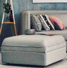 Grey ottoman and couch in room with pink decorative accents