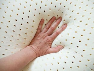 Perforated latex pillow with hand pushing down in the middle