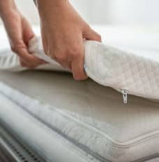 Two hands lifting up the side of a white Mattress Topper