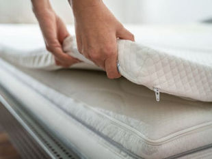 Two hands lifting up the side of a white Mattress Topper