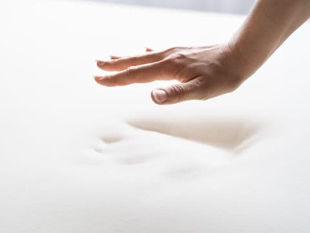 Hand hovering above a white memory foam mattress with a hand indentation