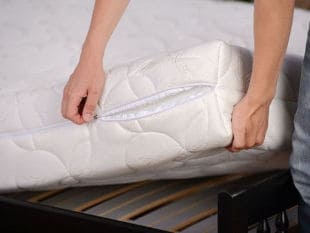 Two hands lifting up white mattress from bed frame