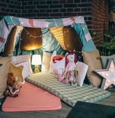 Indoor fort made with blanket with one pink camping mat and one blue patterned camping mat