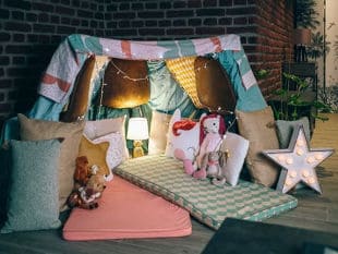 Indoor fort made with blanket with one pink camping mat and one blue patterned camping mat