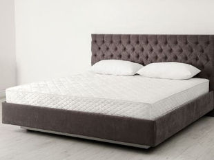 White mattress with two white pillows on top of a brown bed frame with headboard