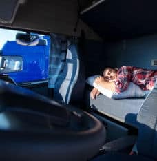 Man asleep on mattress behind the drivers seat in semi-truck