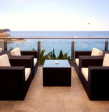 Four black woven chairs with white cushions next to a glass balcony overlooking the ocean