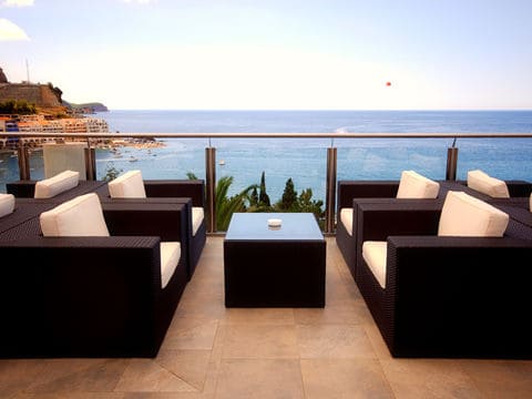 Four black woven chairs with white cushions next to a glass balcony overlooking the ocean