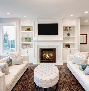 Two white couches facing each other in a living room with a tufted ottoman in the middle of the room