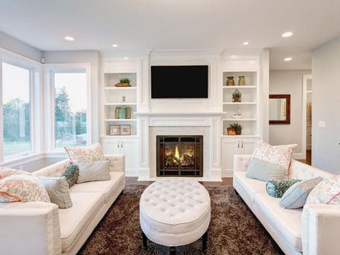 Two white couches facing each other in a living room with a tufted ottoman in the middle of the room