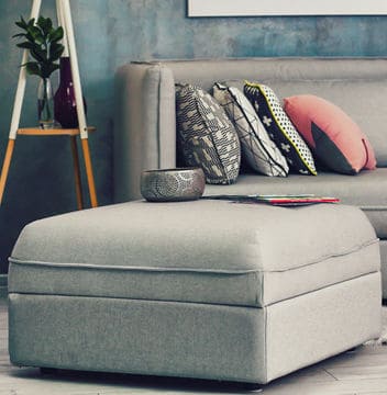 Grey ottoman and couch in room with pink decorative accents