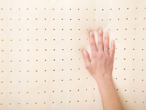 Right hand pressing on top of yellow perforated foam mattress