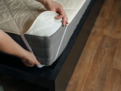 Two hands securing a white mattress cover on a mattress