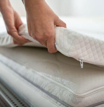 Two hands lifting up the side of a white Mattress Topper