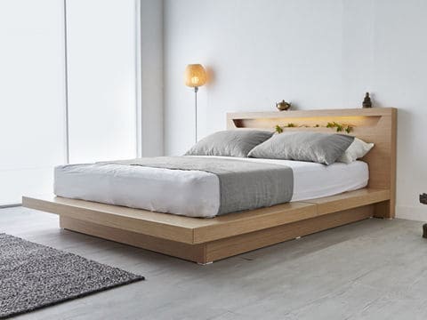 White mattress on a wood base with grey blanket and pillows