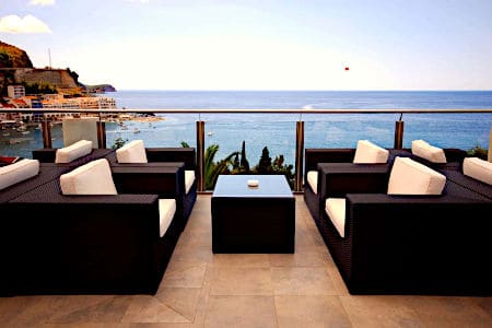 Four black woven chairs with white cushions next to a glass balcony overlooking the ocean