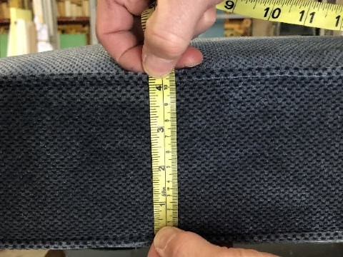 Hands holding measuring tape up against sofa cushion to measure