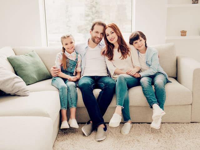 family of 4 sitting closely together on white couch