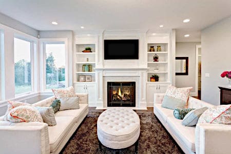 Two white couches facing each other in a living room with a tufted ottoman in the middle of the room