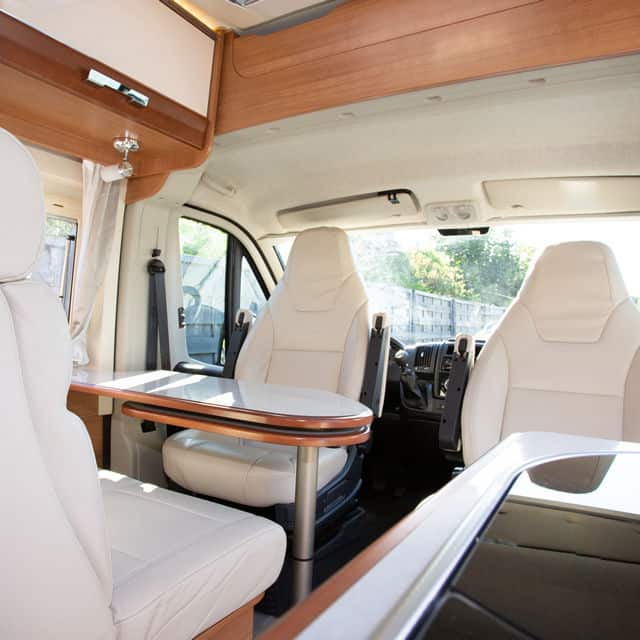 two white rear facing seats in camper van with a wood table