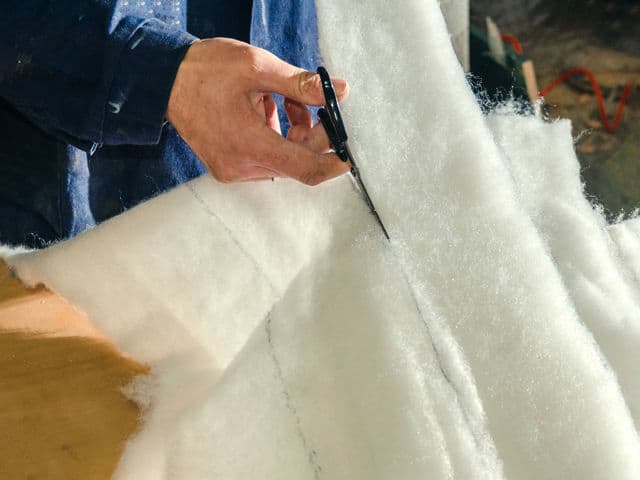 hand holding scissors cutting downwards through white batting