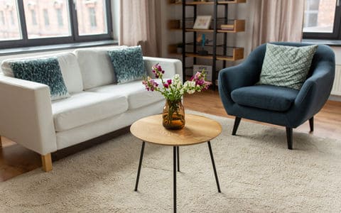 White couch next to a blue chair on a tan run with flowers on a wood table