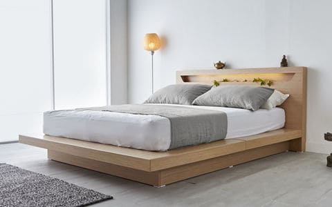White mattress on a wood base with grey blanket and pillows