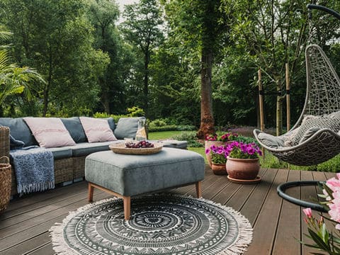 Blue outdoor patio furniture with a hanging seat and ottoman in front of a forest.