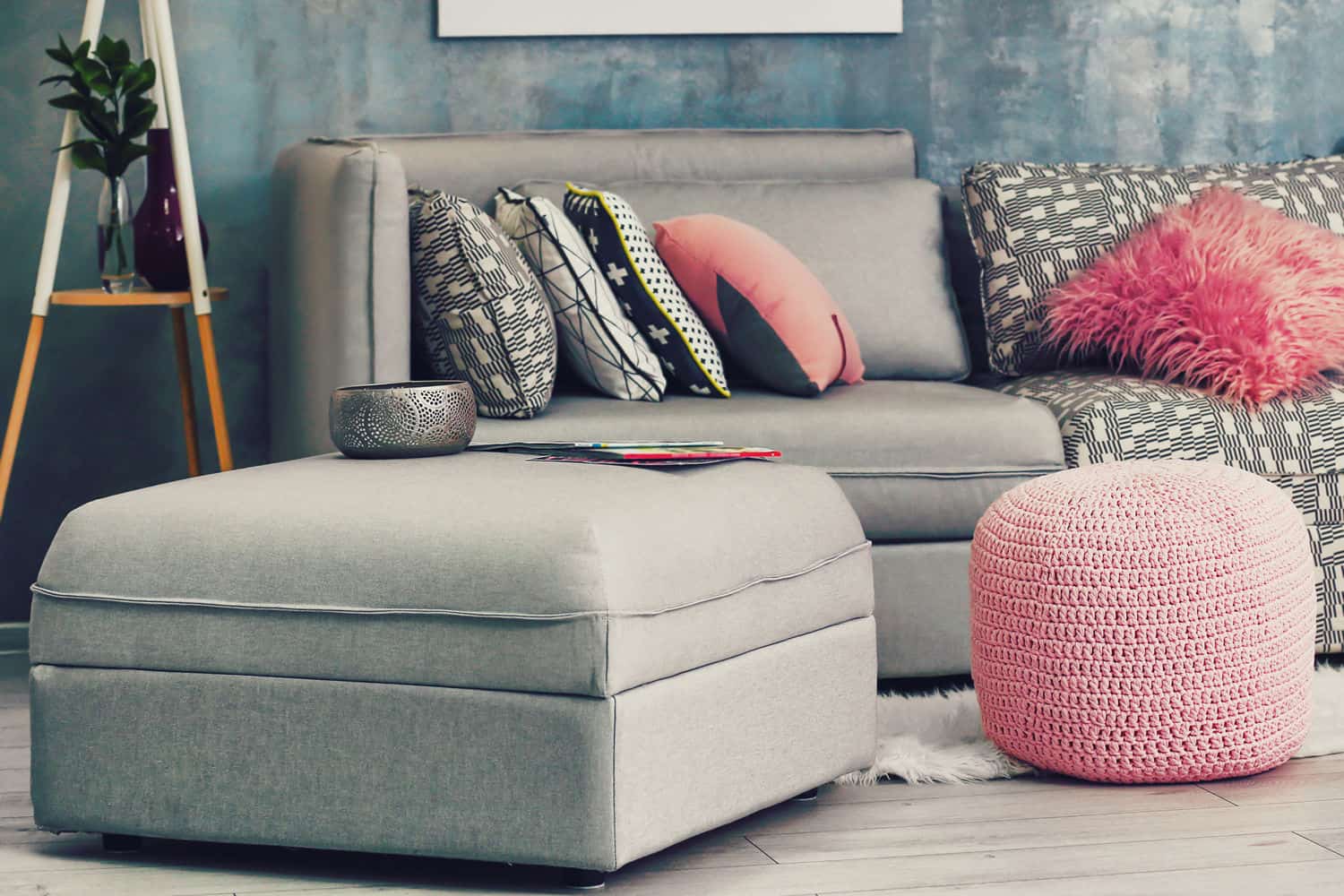 Grey ottoman and couch in room with pink decorative accents