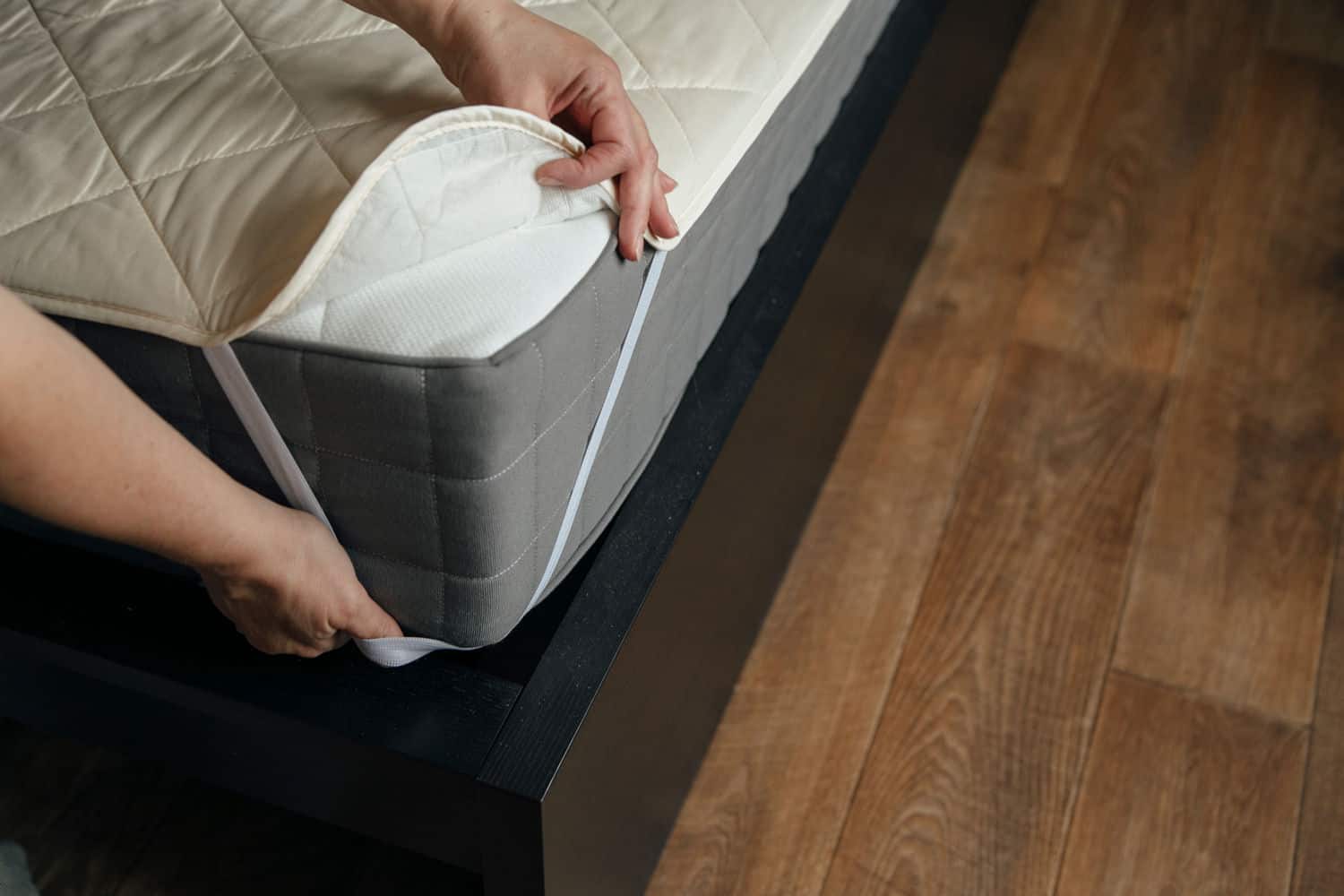 Two hands securing a white mattress cover on a mattress