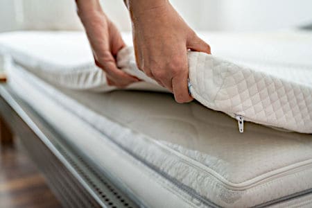 Two hands lifting up the side of a white Mattress Topper