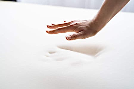 Hand hovering above a white memory foam mattress with a hand indentation