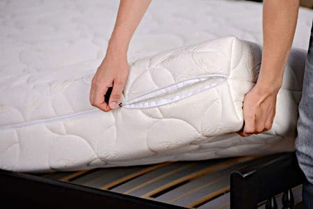 Two hands lifting up white mattress from bed frame