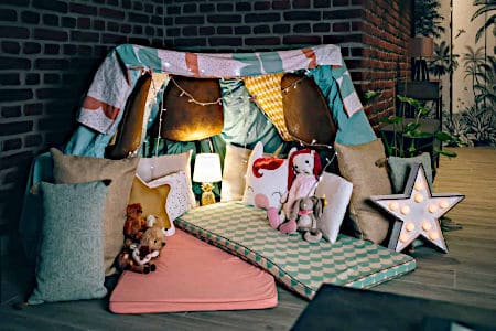 Indoor fort made with blanket with one pink camping mat and one blue patterned camping mat