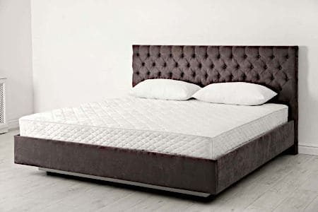 White mattress with two white pillows on top of a brown bed frame with headboard