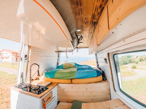 Colorful bedding on mattress inside of a van with door open