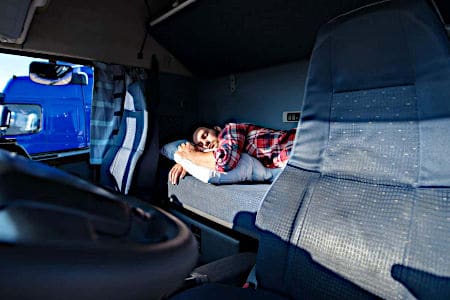 Man asleep on mattress behind the drivers seat in semi-truck